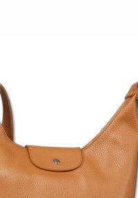 Tan leren schoudertas met een gladde textuur, gebogen ontwerp en een voorflap die is beveiligd met een zilveren knoop, met een enkele schouderriem.