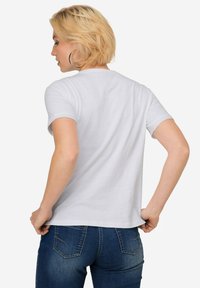 Weißes T-Shirt mit kurzen Ärmeln und Rundhalsausschnitt. Weiches Material, figurbetontes Design. Kombiniert mit dunkelblauen Jeans mit Gesäßtaschen.