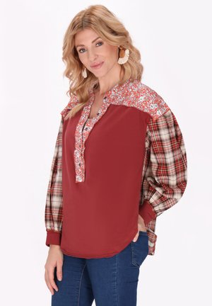 Blusa rossa con yoke a fantasia floreale, maniche a quadri, patta con bottoni e polsini elastici; tessuto leggero con una vestibilità comoda.