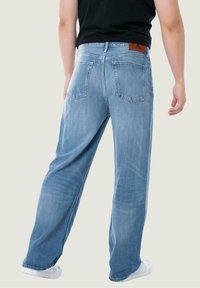 Jeans in denim azzurro chiaro con vestibilità rilassata, dotati di due tasche posteriori e una toppa in pelle marrone sulla cintura.