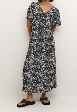 Schwarz-weiß gemustertes Maxikleid mit kurzen Ärmeln, tailliertem Bund und fließender Silhouette. Kombiniert mit schwarzen Flip-Flops.