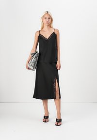 Black camisole with lace trim and matching skirt featuring a lace slit, paired with a snake-print clutch and black sandals.
