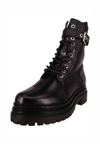 Bota de cuero negra para el tobillo con suela plana, cierre de cordones y correa con hebilla. Presenta un panel lateral texturizado y detalles de costuras resistentes.