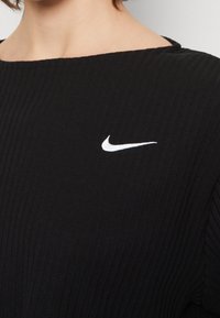 Close-up of a person wearing a black ribbed top with a small white Nike swoosh logo on the chest.