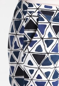 Kjol med ett geometriskt mönster som har blå och svarta trianglar på en vit bakgrund. Tillverkad av tyg med synliga sömmar och sidofickor.