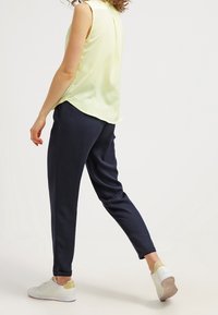 Light yellow sleeveless blouse pairs with navy tapered pants, featuring pockets and a smooth texture, complemented by white sneakers with yellow accents.