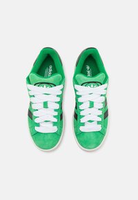 Paire de baskets Adidas en suède vert avec lacets blancs et bandes noires vue de dessus sur fond blanc.