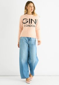 Light pink fuzzy sweater with black "GINI LONDON" text, paired with wide-leg light blue denim jeans and pale pink shoes in a neutral background.