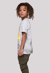 Camiseta de algodón gris con mangas cortas que presenta un diseño gráfico amarillo. Combinada con pantalones cargo verde oliva, con bolsillos visibles y detalles en las costuras.