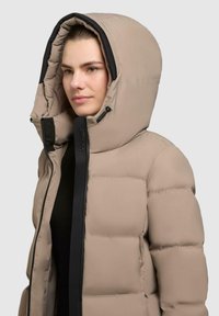 Beige puffer jacket with a large hood, featuring a dark zipper and accents. The fabric is smooth with a glossy finish and quilted design.
