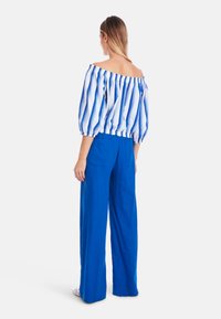 Off-the-shoulder top with blue and white vertical stripes, balloon sleeves, and elastic waist. Paired with high-waisted blue linen trousers.