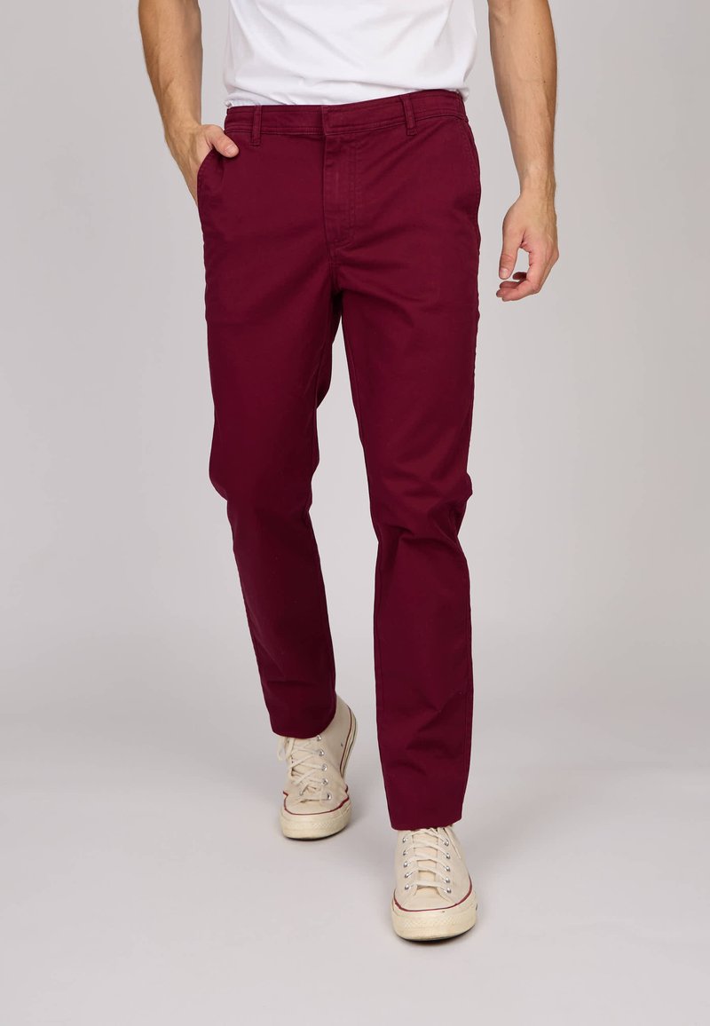 Chinos en coton bordeaux avec une coupe slim, dotés de poches latérales et d'une texture lisse. Portés avec des baskets beiges.