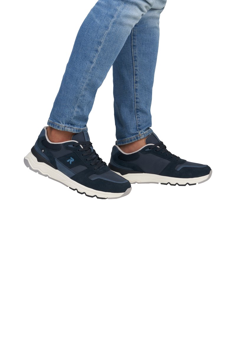 Marinblå sportskor som har en blandning av mocka och nätmaterial, en vit mellansula och en texturerad svart yttersula. Minimal varumärkeslogotyp på sidan.