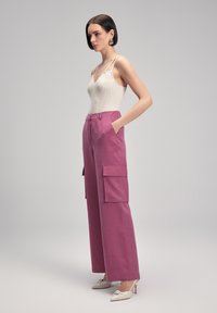 Lichtbeige geribbelde tanktop gecombineerd met hooggerande cargobroek in levendig magenta, met grote zijzakken en een soepele textuur.