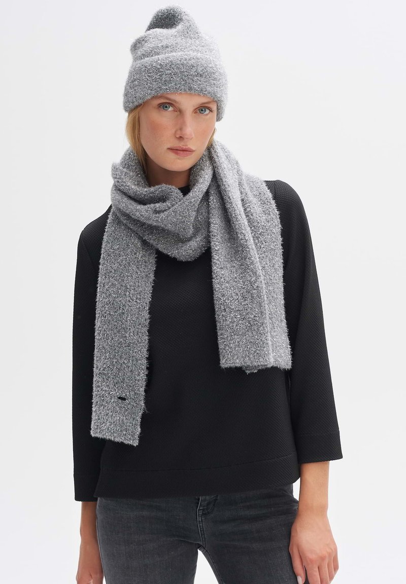 Gray knitted beanie and scarf set, featuring a soft, fuzzy texture. Scarf draped around the neck, with a simple design and no visible hardware.