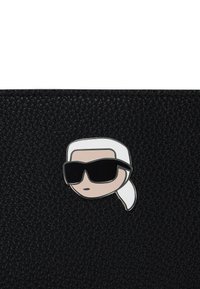 Zwarte leren tas met een gestructureerd oppervlak, voorzien van een cartoonachtige speld van een figuur met wit haar en een zonnebril. De speld is kleurrijk en prominent.