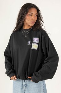 Czarna, oversize bluza z ribbowanym dekoltem i długimi rękawami. Posiada trzy kolorowe naszywki po lewej stronie. Materiał jest miękki i teksturowany.