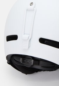 Weißer Skihelm mit aerodynamischem Design, verstellbarem Riemen und schwarzer Innenpolsterung. Mit Belüftungsöffnungen und Logo-Detail.