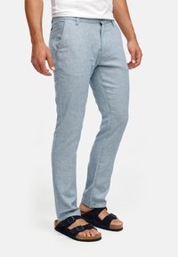 Lichtblauwe, op maat gemaakte broek van een gestructureerde, geweven stof met een gladde afwerking, gecombineerd met donkere sandalen.