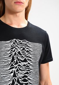 Sort bomulds t-shirt med et hvidt, abstrakt bjergdesign, hvor vandrette linjer skaber et bølge-lignende mønster på stoffet.