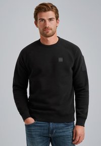 Sudadera negra fabricada con una mezcla de algodón, con un cuello y puños de canalé. Presenta un pequeño parche en el pecho y detalles de bolsillos laterales.