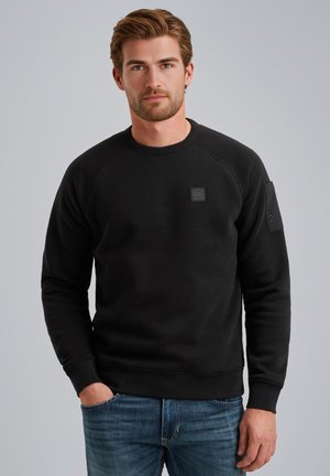 Schwarzes Sweatshirt aus Baumwollmischung mit geripptem Halsausschnitt und Bündchen. Verfügt über einen kleinen Patch auf der Brust und Seitentaschendetails.