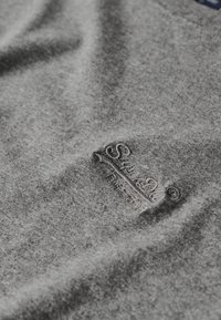 Grijs sweatstof met een zachte textuur, voorzien van een subtiele geborduurde logo op de voorkant, zonder zichtbare patronen of accenten.