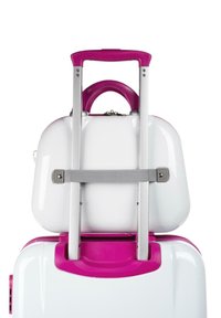 Maleta rígida blanca con asa y detalle en rosa, que cuenta con un carrito de equipaje retráctil de aluminio y una correa de sujeción gris.