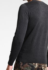 Dark gray pullover sweater with long sleeves, ribbed cuffs, and hem; displayed on a person wearing camouflage pants. Soft, textured fabric.