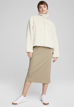 Giacca zip bianca e pelosa con colletto alto, abbinata a una gonna midi a coste beige e sneakers bianche con suole marroni.