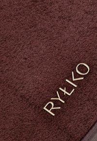 Brązowa tkanina frotte o miękkiej teksturze, z logo w kolorze złotym "RYŁKO" na dole. Skupienie na materiale i kolorze.