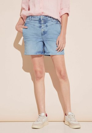 Pantalones cortos de mezclilla azul claro con cierre de cinco botones, bolsillos laterales y un ajuste casual, combinados con zapatillas blancas con acentos rosas.