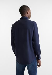 Marineblauwe lange mouw shirt met een kraag, knopenmanchetten en een ronde zoom. Gladde textuur, met een subtiele glans tegen een effen achtergrond.