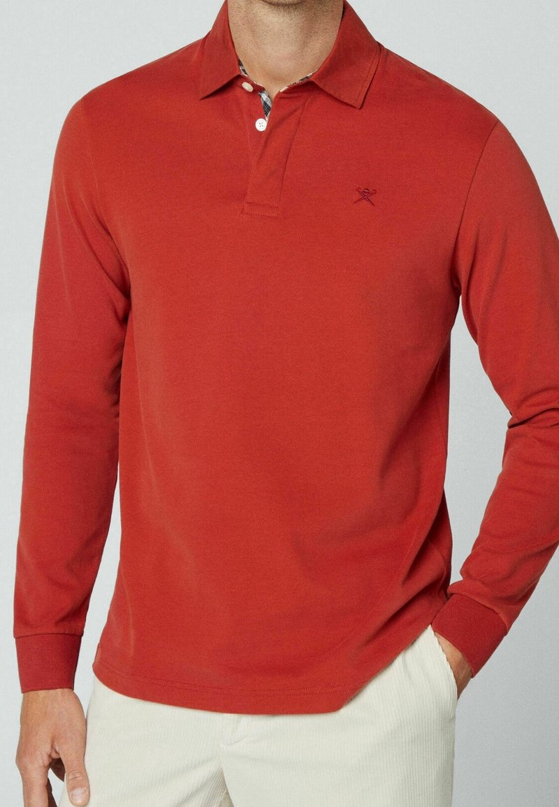 Polo a maniche lunghe rosso con colletto ripiegato e un piccolo logo sul petto, caratterizzato da un sottile motivo a quadri all'interno del colletto.
