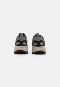 Baskets athlétiques épaisses en gris et noir, avec une tige texturée, un talon renforcé et une semelle robuste avec un motif de crampons prononcé.