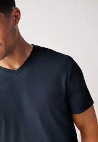 Lyhyet hihat omaava tummansininen V-kaula-aukko T-paita, joka on valmistettu sileästä, kevyestä kankaasta, jossa on hienovarainen kiilto ja siistit ompeleet reunoilla.