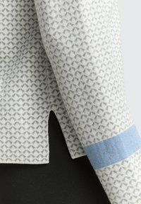 Pull blanc avec motif en losanges gris, featuring une bande bleue sur la manches et une fente sur le côté. Texture douce et coupe décontractée.