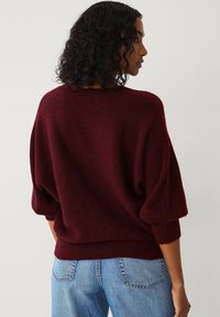Pull en tricot bordeaux à coupe décontractée, manches ballon, encolure large et ourlet côtelé, associé à un jean en denim bleu clair.