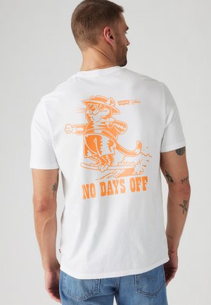 Hvid bomulds t-shirt med et grafik af en tegneseriekat på en skateboard, i orange, med teksten "NO DAYS OFF" under billedet.