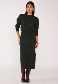 Completo in maglia verde scuro composto da un maglione a coste e una gonna fitted fino al ginocchio, abbinato a stivali marroni alti fino al ginocchio.