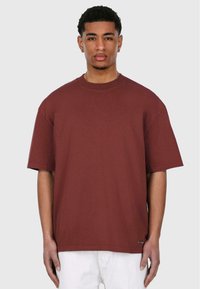 Maroon bomulds t-shirt med korte ærmer, rund halsudskæring, en afslappet pasform og et lille logo mærke i den nederste kant.