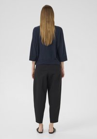 Marineblaues Strickoberteil mit lockerer Passform und dreiviertel Ärmeln, kombiniert mit schwarzen, schmal zulaufenden Hosen. Glatte Textur, lässige Silhouette.