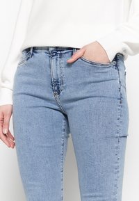 Jeans in denim azzurro chiaro con vita a metà altezza, due tasche frontali e vestibilità classica. Leggero effetto consumato lungo la vita.