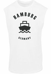 Fehér, ujjatlan póló, amelyen egy fekete grafika látható egy hajóról és hullámokról, a felirat "HAMBURG" a hajó fölött és "GERMANY" alatta, vastag betűkkel.