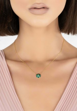 Collana d'oro con un pendente circolare adornato da una pietra preziosa verde. La catena è delicata e completa il design del pendente.