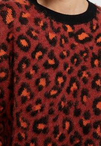 Rode trui met een zachte textuur en een zwart-oranje luipaardprint. Zwarte geribbelde halslijn. Close-up van het stofpatroon.