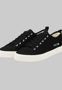 Sneakers neri in tela con suole in gomma bianca, dotati di sei occhielli per i lacci, un dettaglio del logo a contrasto e un design leggero e texturizzato.