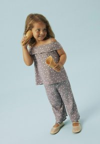 Haut gris à épaules dénudées avec des pois blancs, associé à un pantalon à pois assorti et des chaussures beiges à enfiler. Enfant tenant deux cornets de glace.