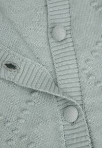 Jasnoszary sweter z dzianiny z prążkowanym kołnierzem, dwiema okrągłymi guzikami i teksturowanymi wzorami na tkaninie. Widoczna jedna mała dziura.