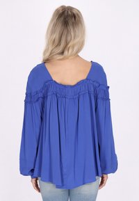 Blusa blu scollata sulle spalle con dettagli arricciati lungo il collo e maniche lunghe fluide, realizzata in un tessuto leggero.